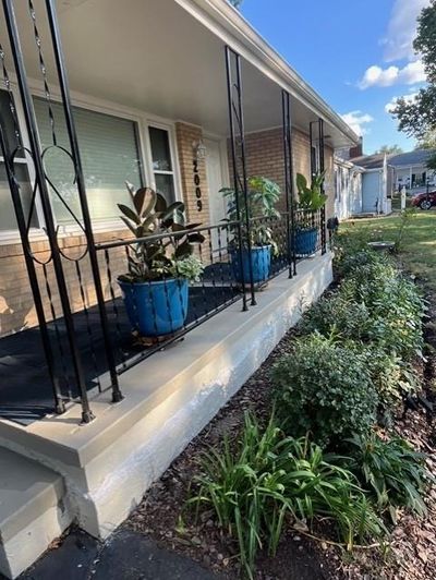 Single story home with a double wide driveway that extends behind the fence, a one car garage, and covered porch | Image 1