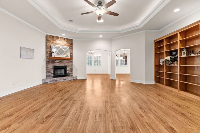 Unfurnished living room with arched walkways, ornamental molding, a ceiling fan, visible vents, and a raised ceiling | Image 5