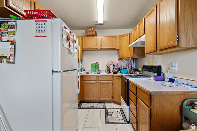 Kitchen featuring freestanding refrigerator, black electric range, under cabinet range hood, light countertops, and light tile patterned floors | Image 13