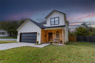 View of front facade featuring a yard, covered porch, and a garage | Image 1