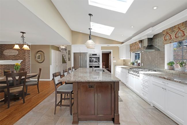 Kitchen with a breakfast bar, a fireplace, vaulted ceiling with skylight, appliances with stainless steel finishes, and wall chimney range hood | Image 12