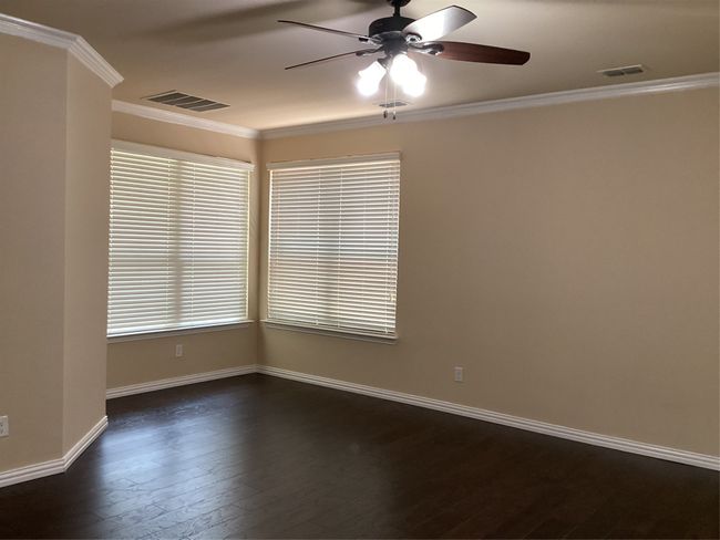Empty room with a ceiling fan, ornamental molding, dark wood-style floors, and baseboards | Image 12