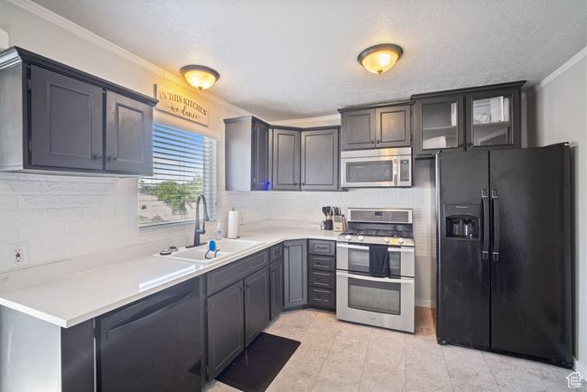 Kitchen with appliances with stainless steel finishes, a sink, ornamental molding, decorative backsplash, and light countertops | Image 4