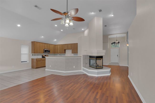 Unfurnished living room with ceiling fan, light wood-style floors, lofted ceiling, a multi sided fireplace, and recessed lighting | Image 10