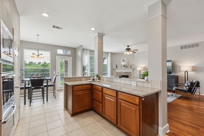 Kitchen with open floor plan, a fireplace, ornate columns, ceiling fan, and brown cabinetry | Image 9