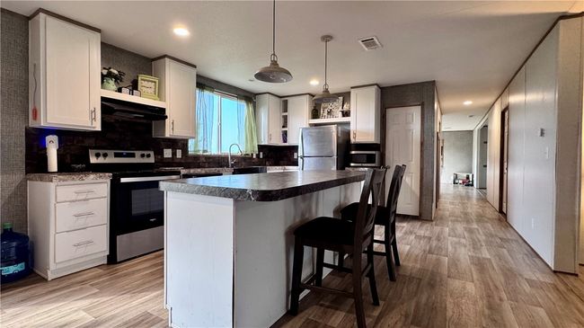 Kitchen with open shelves, stainless steel appliances, white cabinets, a breakfast bar, and recessed lighting | Image 10