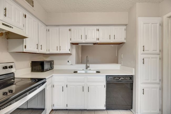 Kitchen featuring black appliances, a textured ceiling, white cabinetry, light countertops, and light tile patterned floors | Image 9