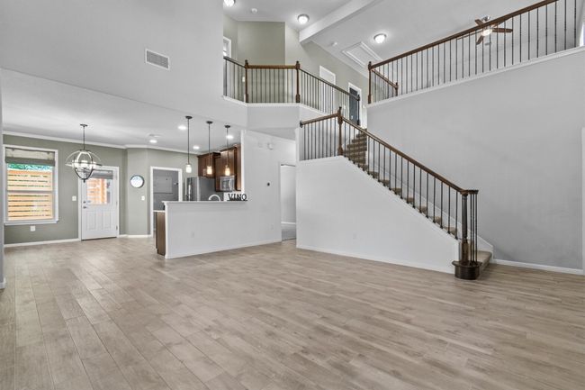 Unfurnished living room with a chandelier, a towering ceiling, light wood-type flooring, stairway, and baseboards | Image 10