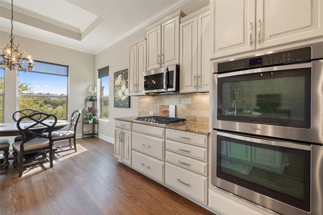 Kitchen with decorative backsplash, dark wood-style flooring, appliances with stainless steel finishes, light stone countertops, and a chandelier | Image 11