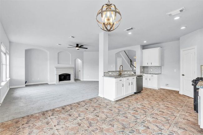 This open-concept living area features a modern kitchen with granite countertops and stainless steel appliances, a spacious living room with a cozy fireplace, and a mix of carpet and tile flooring. Natural light flows in through large windows, enhancing the airy feel. | Image 11