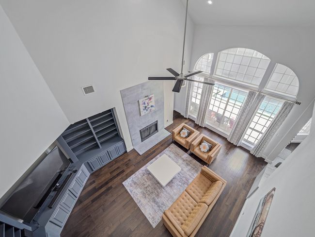 Living area with a tiled fireplace, a high ceiling, wood finished floors, a ceiling fan, and recessed lighting | Image 16