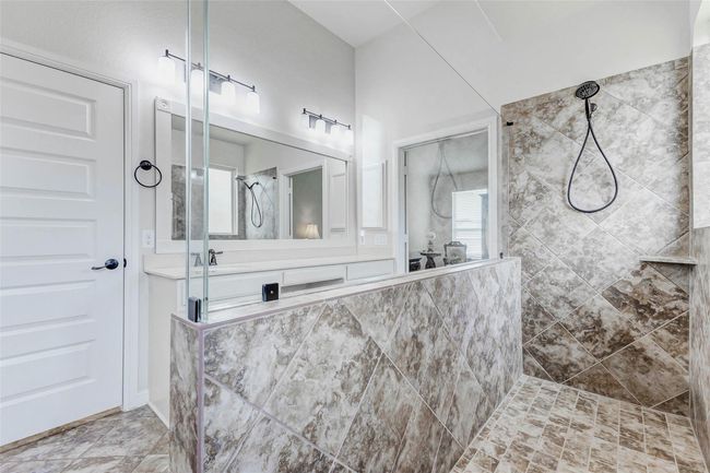 A closer look at the walk-in shower showcases the beautiful neutral tile surround and bronze fixtures. A rain glass window floods the space with natural light, enhancing its tranquil ambiance. | Image 19