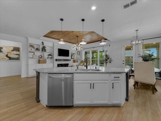 Kitchen featuring dishwasher, a chandelier, a sink, light wood finished floors, and white cabinetry | Image 6
