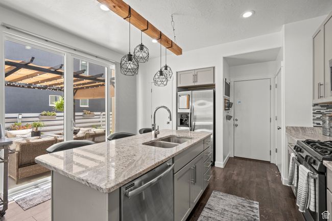 Kitchen featuring gray cabinetry, stainless steel appliances, an island with sink, light stone counters, and recessed lighting | Image 12