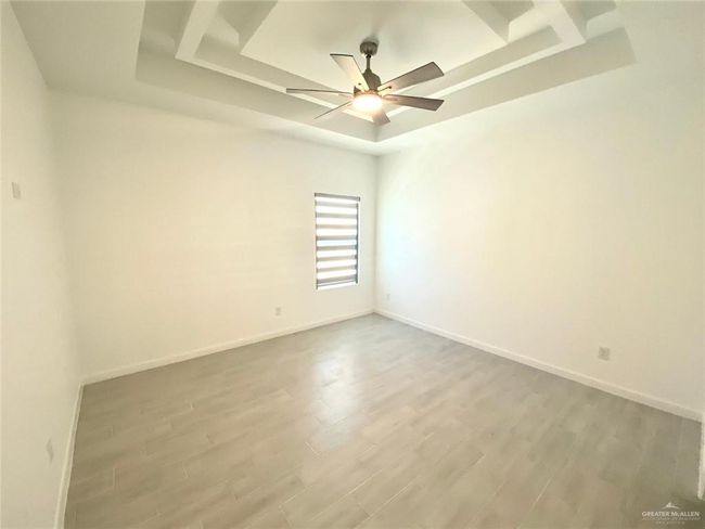 Empty room with a tray ceiling, wood finished floors, and ceiling fan | Image 7