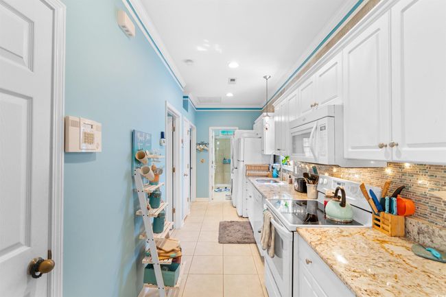 Kitchen featuring white appliances, light tile patterned flooring, decorative backsplash, white cabinetry, and ornamental molding | Image 13