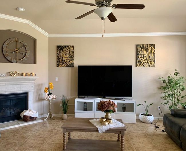 Living room with baseboards, crown molding, a ceiling fan, tile patterned flooring, and a tile fireplace | Image 12