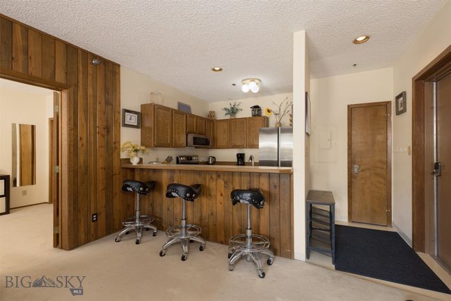 Kitchen with kitchen peninsula, light colored carpet, a kitchen bar, wooden walls, and appliances with stainless steel finishes | Image 13