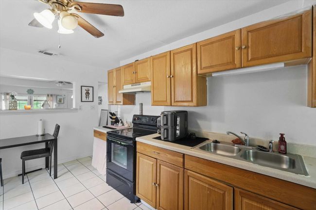 Kitchen featuring visible vents, black electric range oven, a sink, light countertops, and under cabinet range hood | Image 9