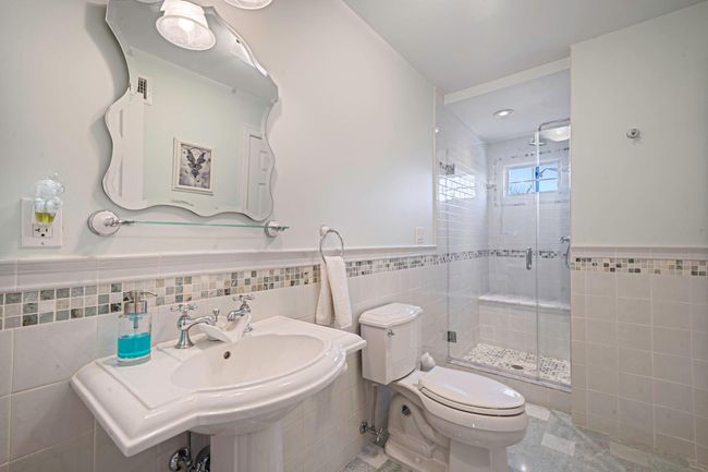 Full bath featuring toilet, a wainscoted wall, a stall shower, and tile walls | Image 12