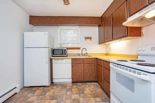 Kitchen with white appliances, baseboard heating, under cabinet range hood, light countertops, and stone finish flooring | Image 8