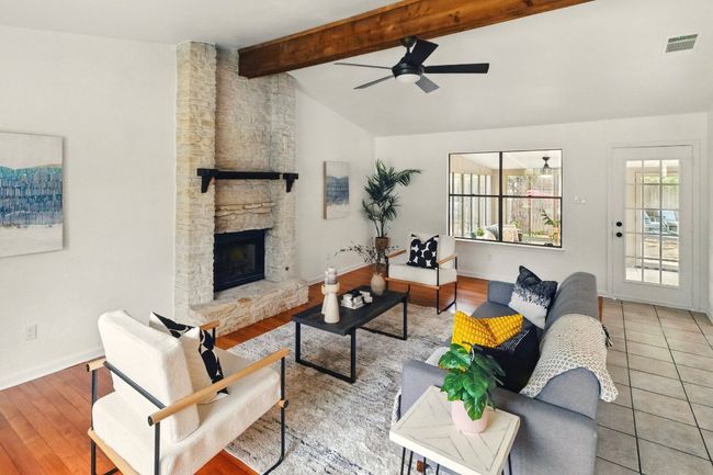 Open-concept living area with vaulted ceilings, a striking wooden beam, and a floor-to-ceiling stone fireplace. Refinished hardwood floors round out the living room space. | Image 6