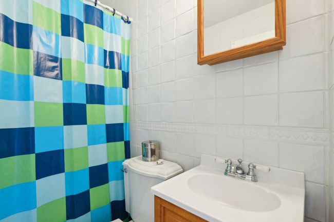 Bathroom with tile walls, vanity, curtained shower, and toilet | Image 16