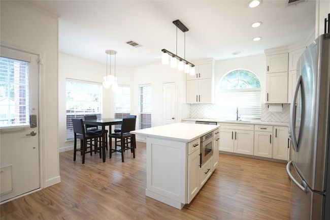 Kitchen with appliances with stainless steel finishes, decorative backsplash, white cabinets, a kitchen island, and pendant lighting | Image 4