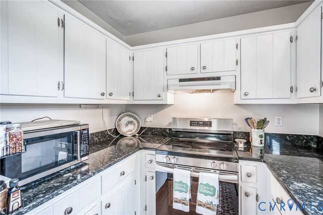 Kitchen with stainless steel appliances, a textured ceiling, dark stone countertops, custom range hood, and white cabinetry | Image 10