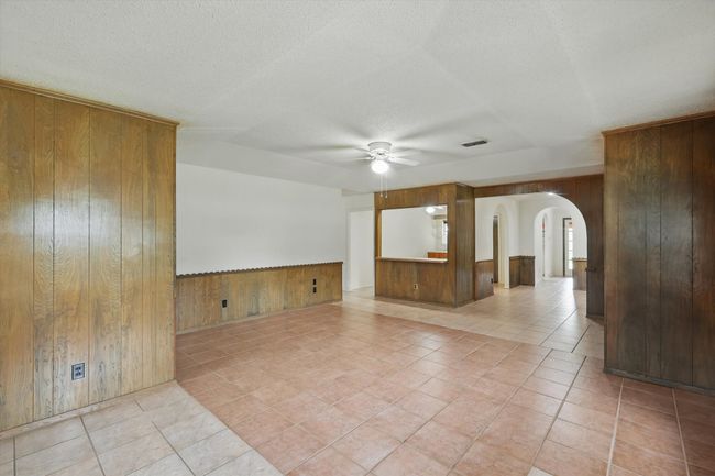 Spare room featuring wood walls, a ceiling fan, arched walkways, light tile patterned flooring, and a wainscoted wall | Image 13