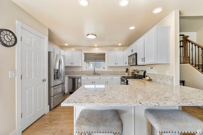 Kitchen with light stone counters, stainless steel appliances, a sink, a peninsula, and a breakfast bar area | Image 12
