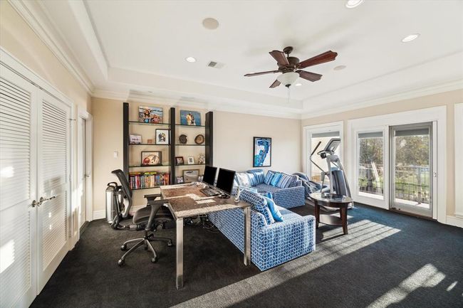 This spacious, well-lit extra room features built-in shelves, and a cozy seating area. Large windows and glass doors offer ample natural light and views of the outdoors. | Image 19