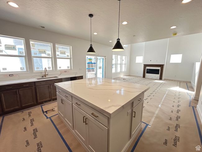 Kitchen featuring recessed lighting, a center island, a textured ceiling, decorative light fixtures, and a glass covered fireplace | Image 7