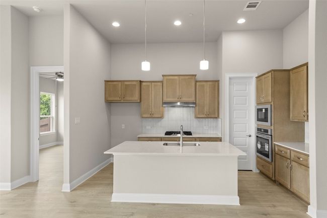 Kitchen with appliances with stainless steel finishes, under cabinet range hood, tasteful backsplash, a towering ceiling, and a center island with sink | Image 17