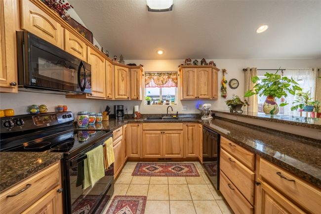 Kitchen with black appliances, light tile patterned floors, dark stone countertops, and a sink | Image 4