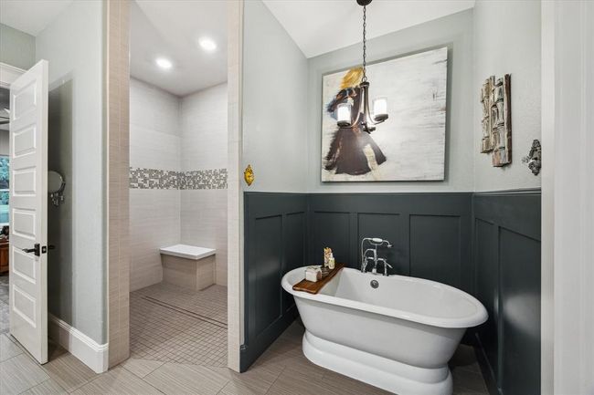 The in-law suite’s primary bathroom is designed for both function and luxury, featuring a wheelchair-accessible walk-in shower with grab bars and a shower bench. A stunning chandelier hangs over the soaker tub, adding a touch of elegance. Additional amenities include a linen closet and beautiful block paneling, making this space both practical and inviting. | Image 38