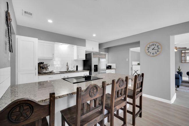 Kitchen featuring a sink, a breakfast bar, black electric cooktop, stainless steel refrigerator with ice dispenser, and visible vents | Image 15