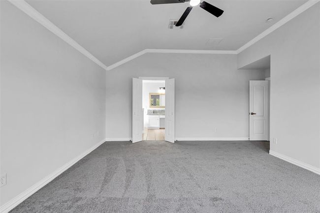 Spacious bedroom with neutral gray walls and carpet, featuring high ceilings and a modern ceiling fan. Double doors open to a bright adjoining bathroom, enhancing the room's airy feel. | Image 28