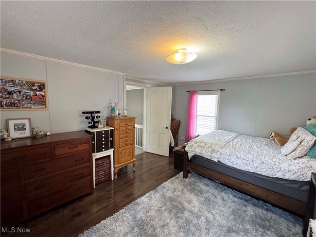 Bedroom with ornamental molding, dark wood-style flooring, and a textured ceiling | Image 25
