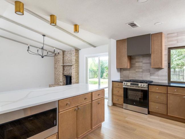 Kitchen with stainless steel range with gas cooktop, beam ceiling, light stone countertops, tasteful backsplash, and light wood-style flooring | Image 15