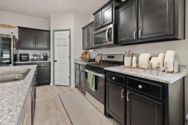 Kitchen featuring stainless steel appliances, light ceramic tile flooring, dark cabinets, and light granite countertops | Image 13