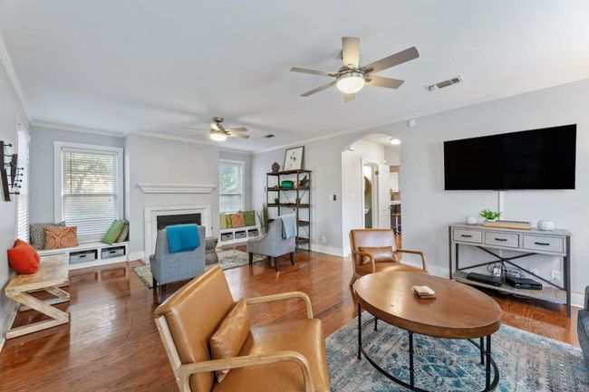 Living room featuring ceiling fan, arched walkways, crown molding, a fireplace, and wood finished floors | Image 6