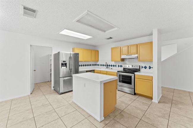 Kitchen featuring appliances with stainless steel finishes, under cabinet range hood, a sink, a textured ceiling, and light brown cabinets | Image 13