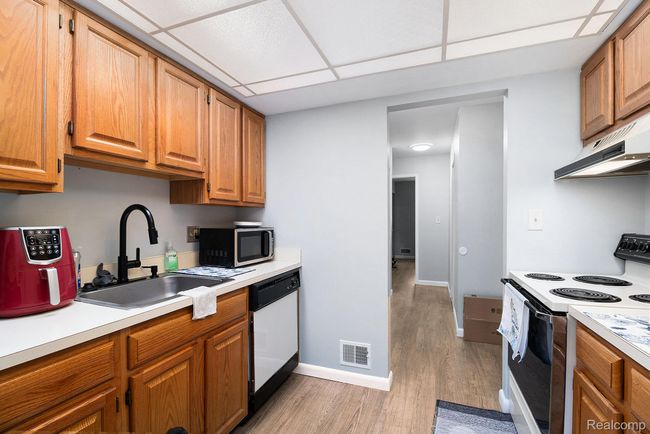 Kitchen with range with electric cooktop, light countertops, a paneled ceiling, light wood-type flooring, and white dishwasher | Image 11
