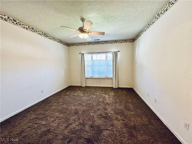 Empty room featuring baseboards, dark colored carpet, ceiling fan, and a textured ceiling | Image 13