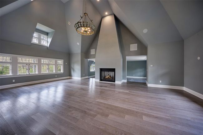 Unfurnished living room featuring a chandelier, high vaulted ceiling, wood finished floors, and baseboards | Image 11