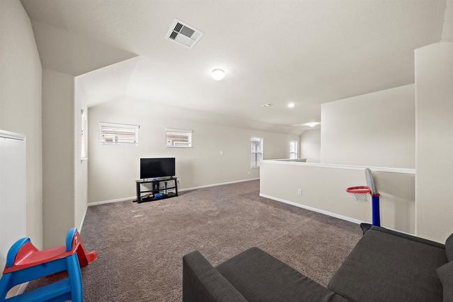 This spacious, carpeted Game room features neutral walls, recessed lighting, and multiple small windows for natural light. It includes a cozy TV area and is ideal for a family space or entertainment room. | Image 16