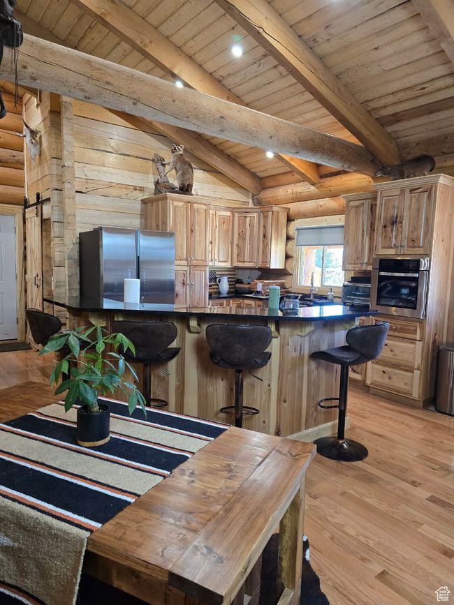 Kitchen featuring rustic walls, light wood-type flooring, beam ceiling, and appliances with stainless steel finishes | Image 57