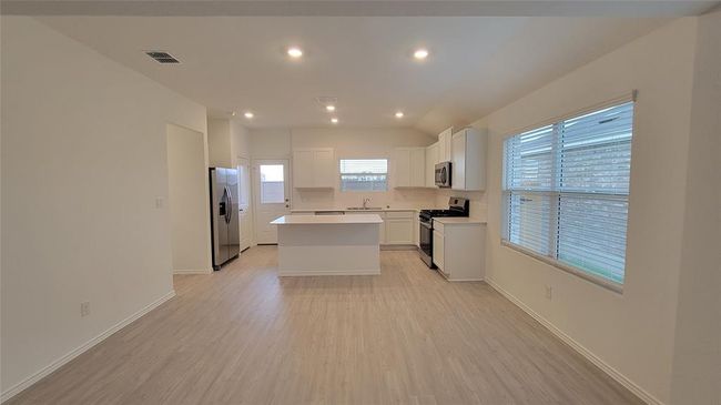 Kitchen with stainless steel appliances, light wood-style floors, white cabinetry, a center island, and light countertops | Image 6