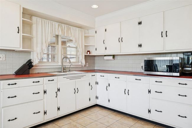 Kitchen featuring white cabinetry, open shelves, stainless steel microwave, and a sink | Image 22